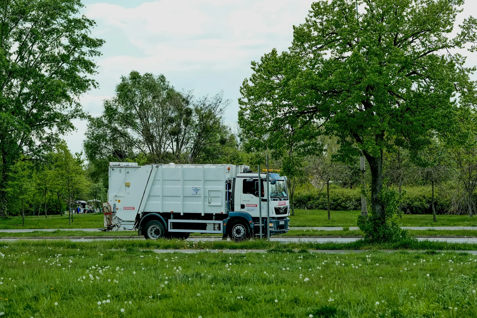 Avfallsbil i ett grönt stadslandskap.