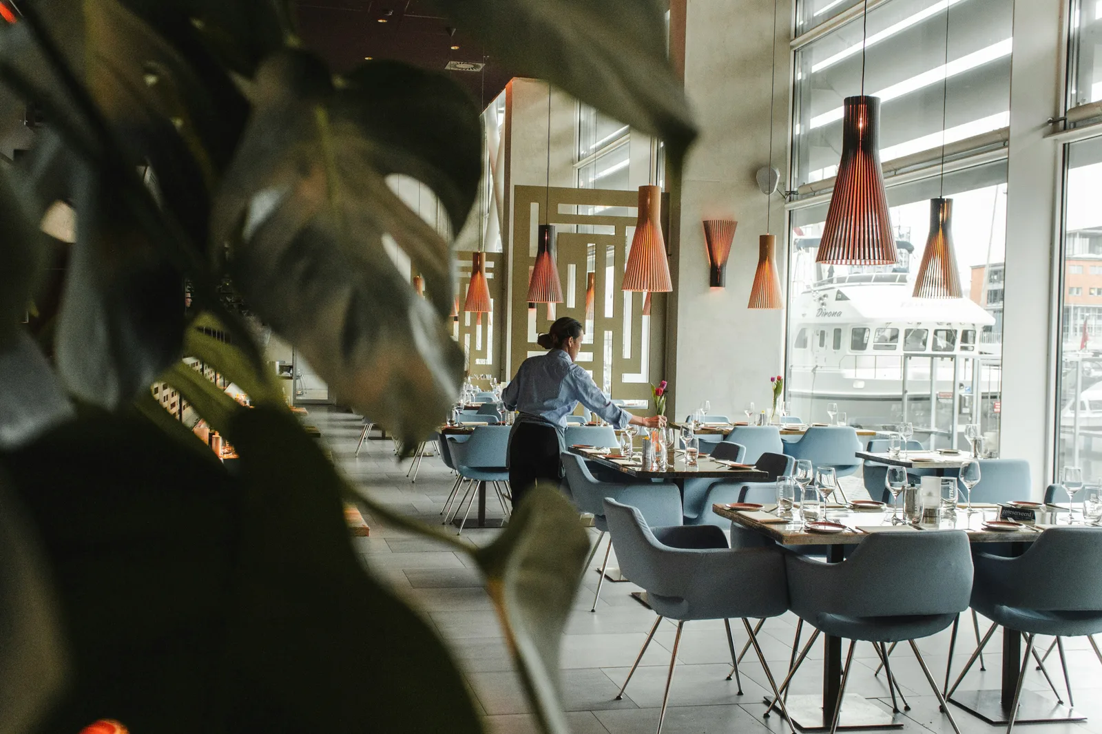 Servitör förbereder dukade bord i en modern hamnrestaurang.